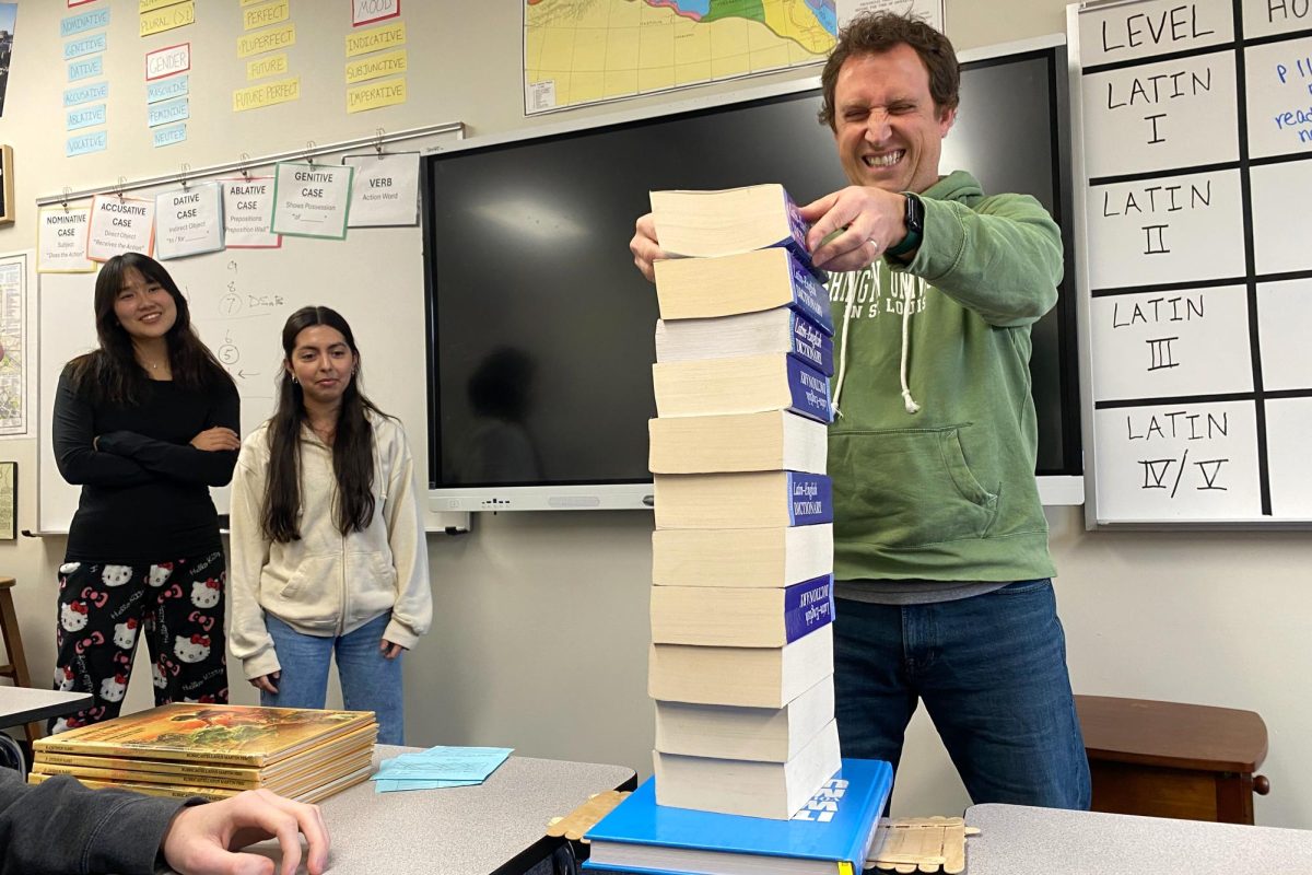 Hearing the bridge creak, Latin teacher Tom Herpel winces as he carefully stacks another book on top of a popsicle stick bridge during Latin 3 on Feb. 7. Within groups, students were randomly assigned different hierarchical roles of Ancient Roman construction workers and attempted to build bridges for their Roman Engineering unit. “I created this activity to showcase how certain [Romans] on a construction site would not talk to each other because they were higher or lower in society, and that creates problems when trying to create a final product. So then, after [the students’] bridges were done, we tested how strong they were. We slowly put more and more books onto the bridge to see when the bridge would break. And believe it or not, that bridge got to the point where someone actually sat on it,” Herpel said.