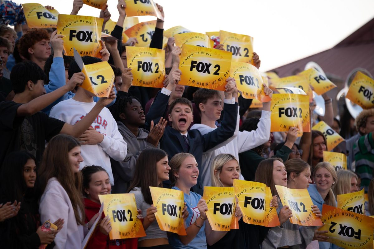 Dressed professionally in a suit and tie, sophomore Eric Thomas cheers with the crowd at the pep rally on Oct. 3. Thomas held up a Fox 2 News poster and celebrated his first time being on the news. “It was pretty interesting, because I've never seen a news crew in person before. Seeing their giant camera set up was pretty cool. The atmosphere was super energetic, which [was] definitely my favorite part, “ Thomas said. 