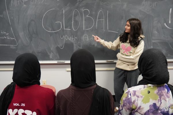 Gesturing toward the club’s name on the board, Global Youth Aid co-president year Daniah Alsagheer discusses upcoming service projects with members during a meeting on Oct. 30. “We might be one club at one school, but together, we’re [part of] something much bigger,” Alsagheer said.
