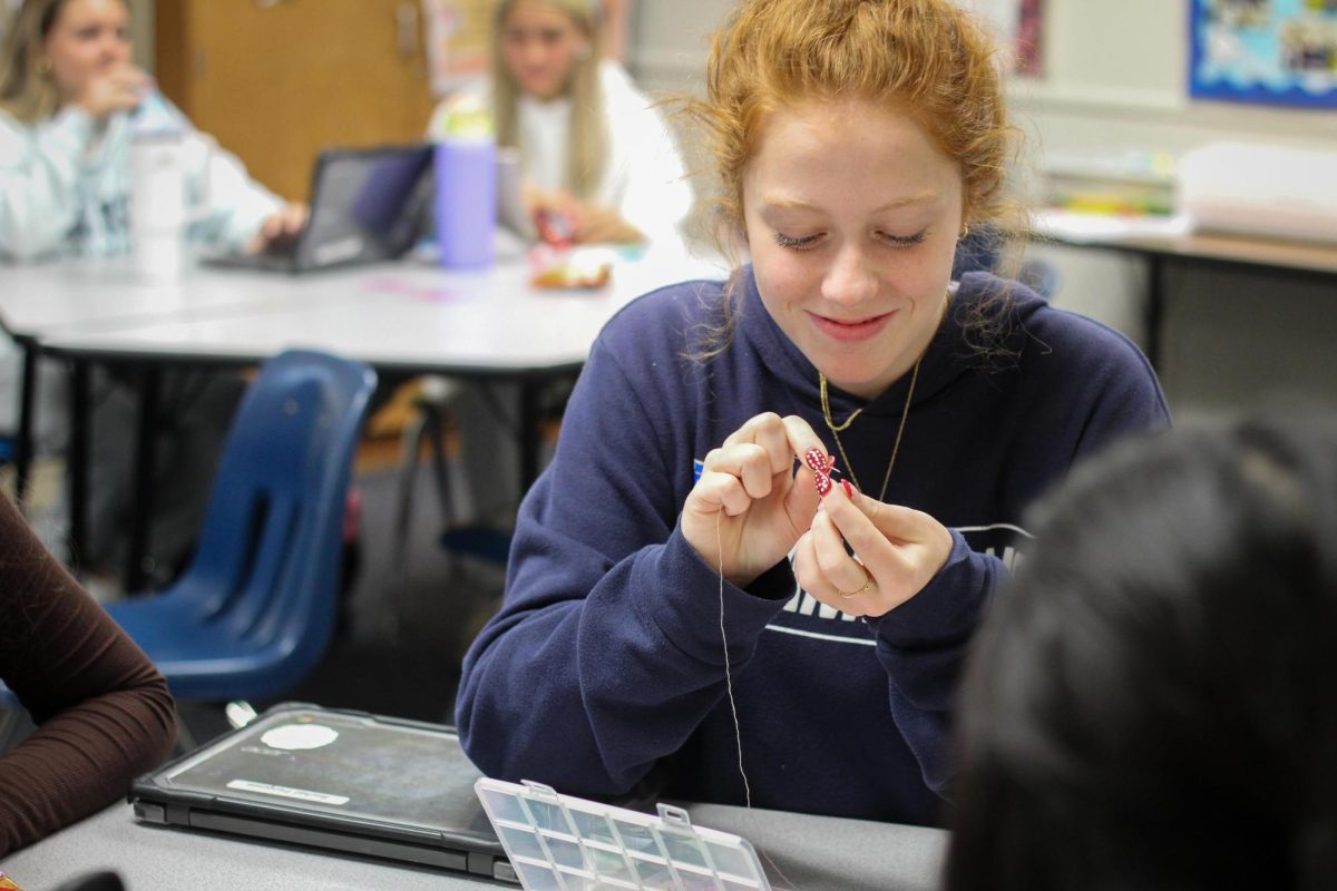 Focusing on the pattern of her bracelet, Bracelet Club leader and senior Lily Maley creates a design during a monthly meeting. Club members use bead packs to create whatever they would like in the moment. "I decided to create this club with my friend because we started making bracelets [in the library] and everybody kind of joined in. I have pride because I created a club that other people get to go to. I think Bracelet Club matters because it brings people together, and it's just a fun time,” Maley said.