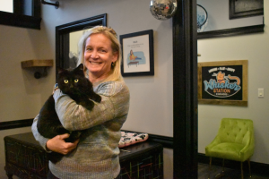 Holding Mr. Ray, Alumna Sara McGinnis poses for a photo inside the Whisker Station Cat Cafe and Lounge. Created in 2020, the cafe serves as a safe space for foster cats, as well as a fun place for people to visit. “A lot of people come here to spend some time [playing] with the cats, especially if they don’t or can’t have them,” McGinnis said.